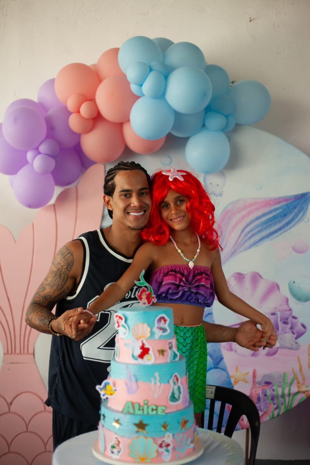 Um adulto e uma menina juntos ao lado do bolo de aniversário.