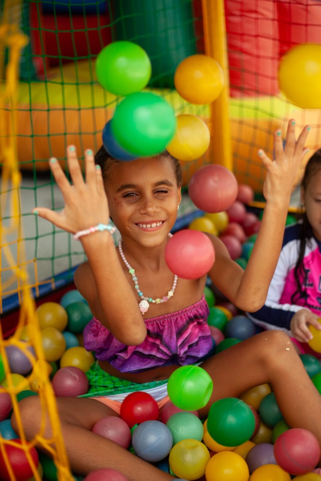 Menina brincando em uma piscina de bolinhas coloridas durante a festa.